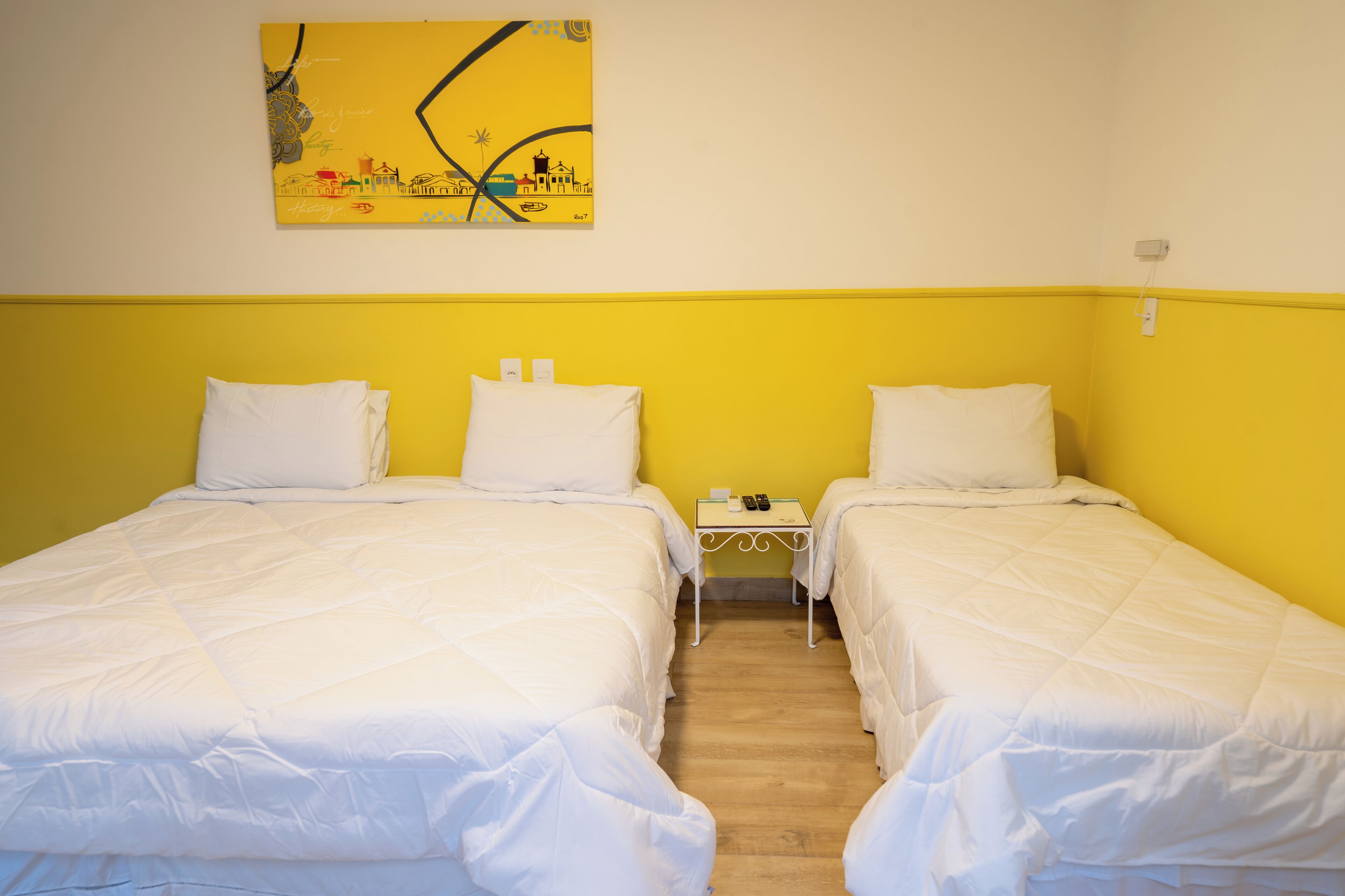 Een hotelkamer met twee bedden, een klein nachtkastje met een telefoon en een kopje, en een schilderij aan de muur.