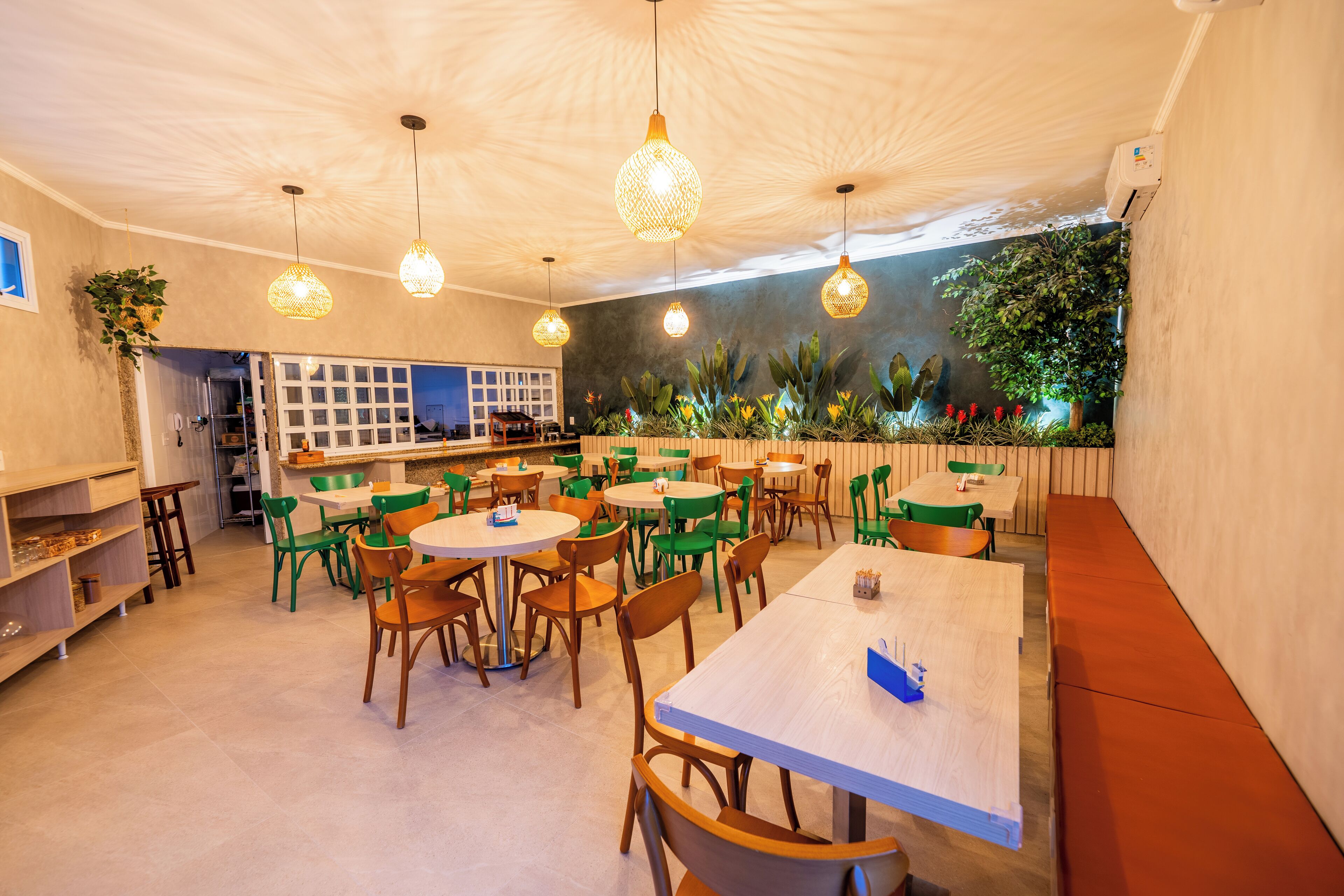 Un restaurante con mesas redondas, sillas verdes y anaranjadas, y lámparas colgantes.