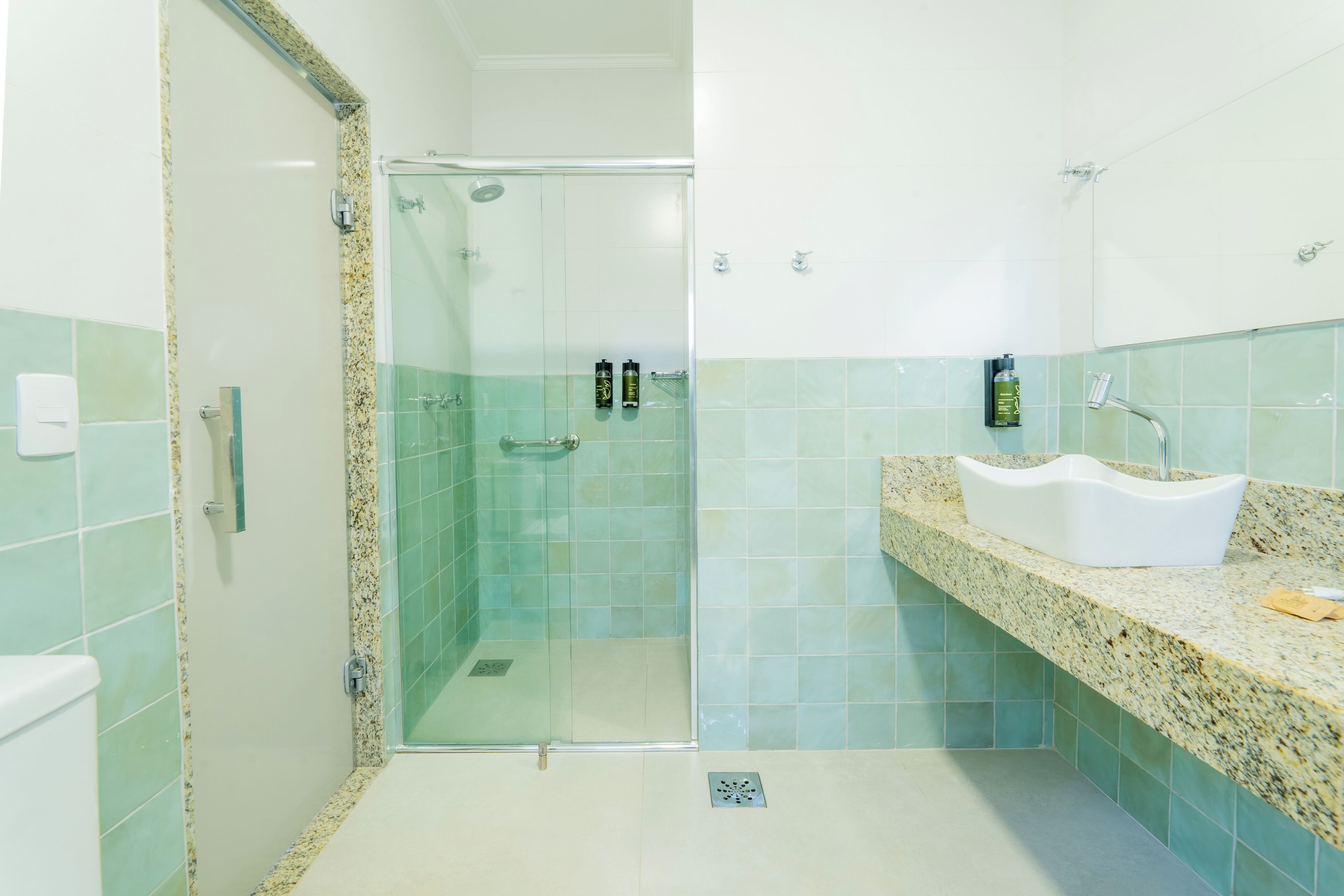 Un baño con ducha envuelta en vidrio, un lavabo blanco y paredes con azulejos verdes.