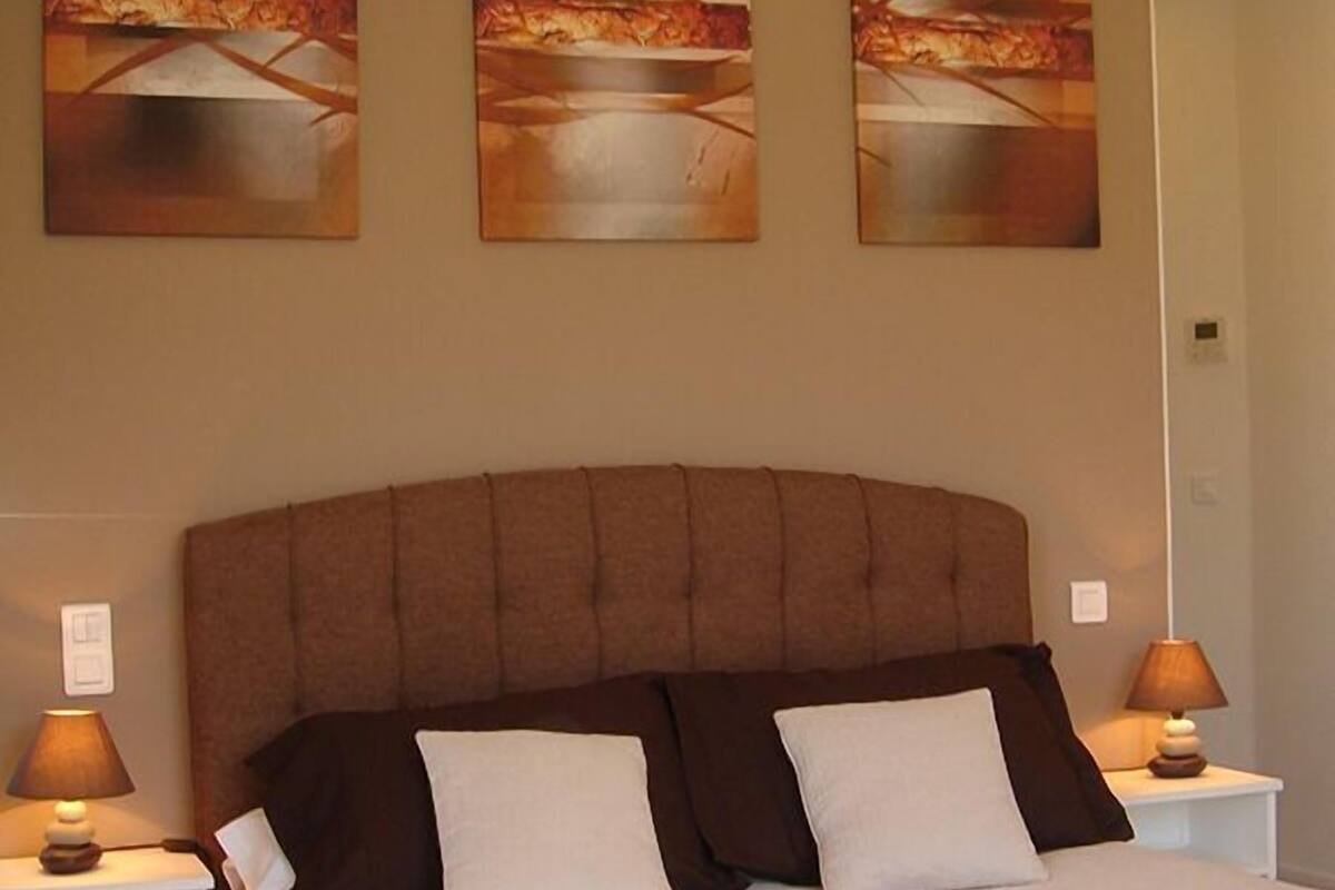 A bedroom with a large bed, two bedside tables, and three abstract paintings on the wall.