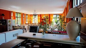 A spacious kitchen with a central island, a dining area with a red tablecloth, and a large window with orange curtains. - Auberge Provencale (Sospel)