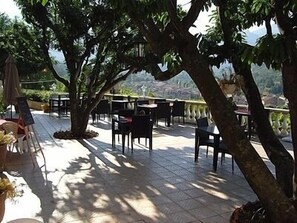 An outdoor patio area with tables and chairs, surrounded by trees and overlooking a scenic landscape. - Auberge Provencale (Sospel)