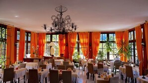 A dining area with tables set for guests, large windows with orange curtains, and a chandelier. - Auberge Provencale (Sospel)