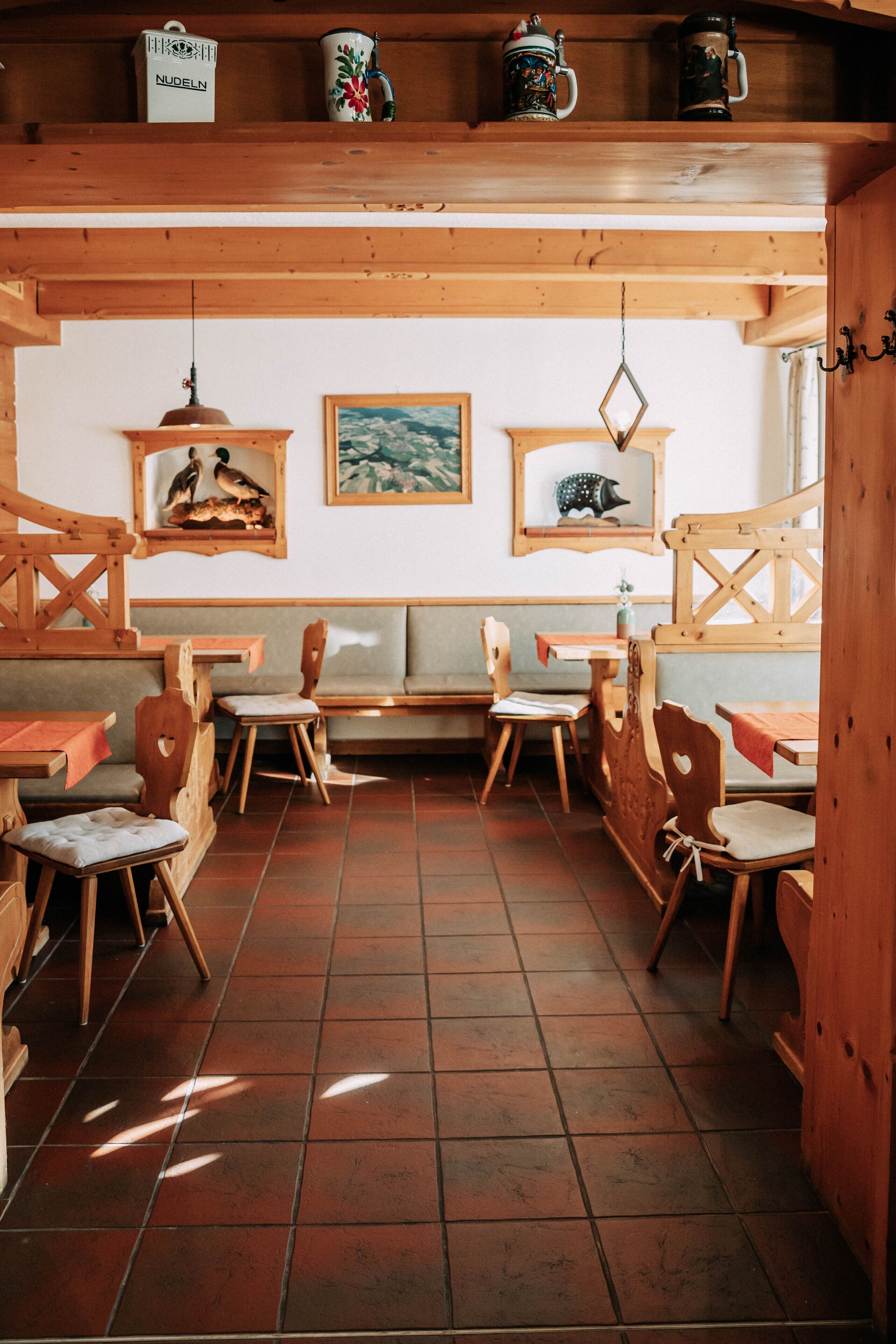 Un interior rústico de madera con bancos y mesas de madera, suelo de baldosas y adornos en la pared, incluyendo cuadros enmarcados.