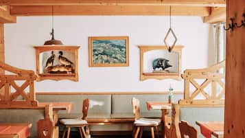 Un interior rústico de madera con bancos y mesas de madera, suelo de baldosas y adornos en la pared, incluyendo cuadros enmarcados.