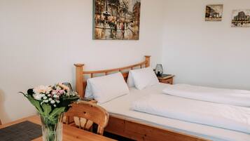 Ein Zimmer mit einem hölzernen Bett, weißer Bettwäsche, einem Nachttisch aus Holz, einer Vase mit Blumen und einem Gemälde an der Wand.