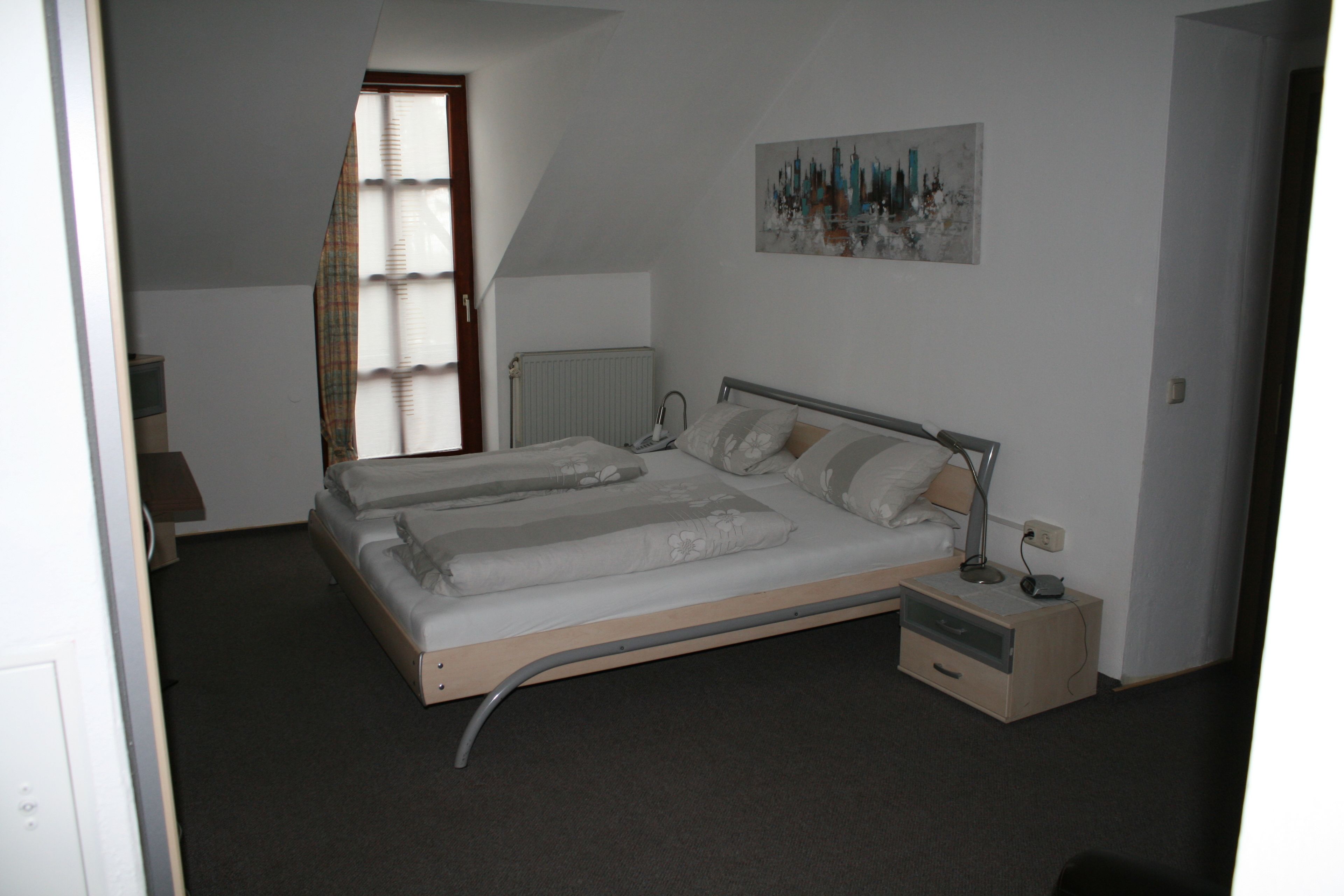 A bedroom with a bed, bedside table, lamp, and a painting on the wall.