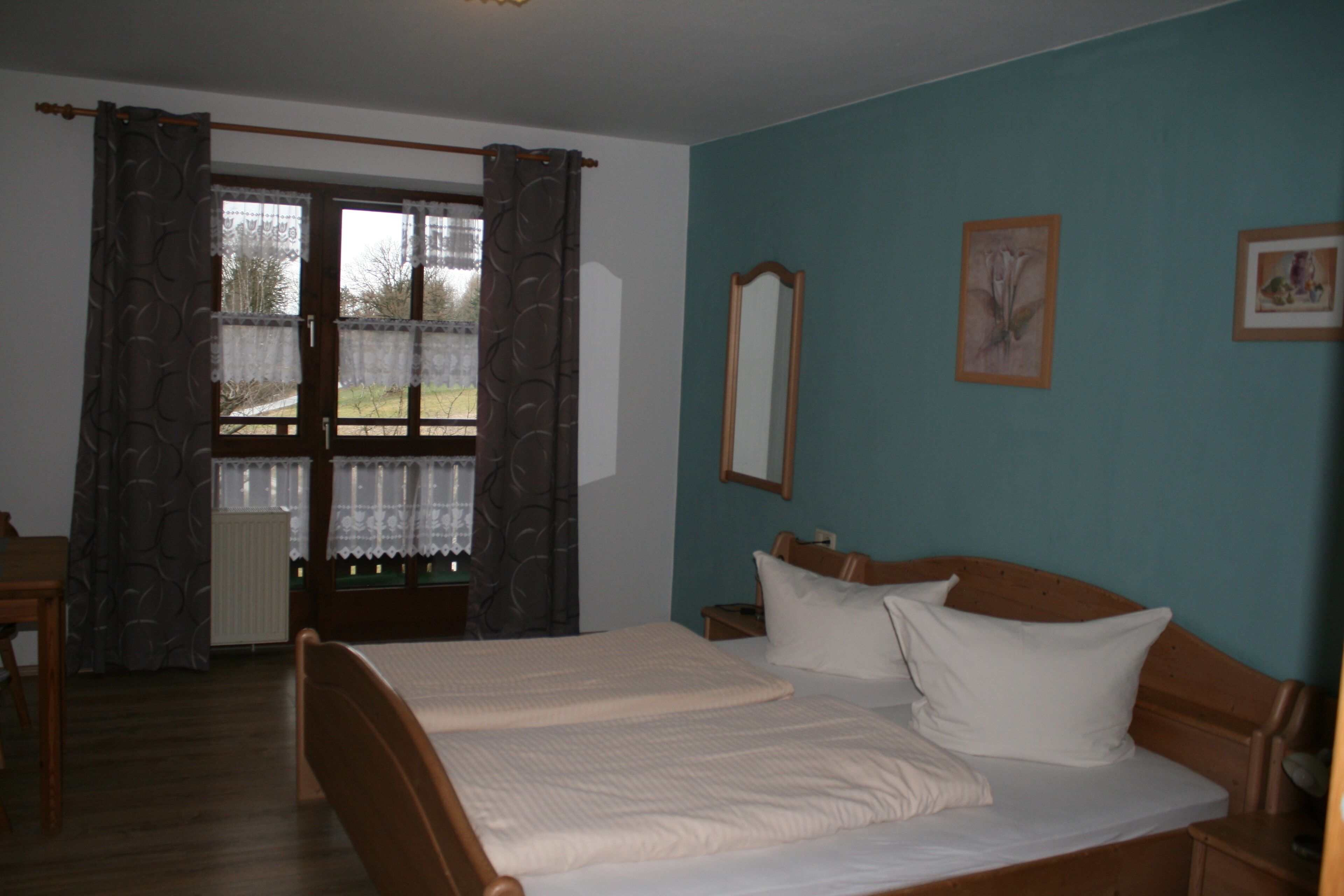 A bedroom with two beds, a window with curtains, a mirror, and a picture on the wall.