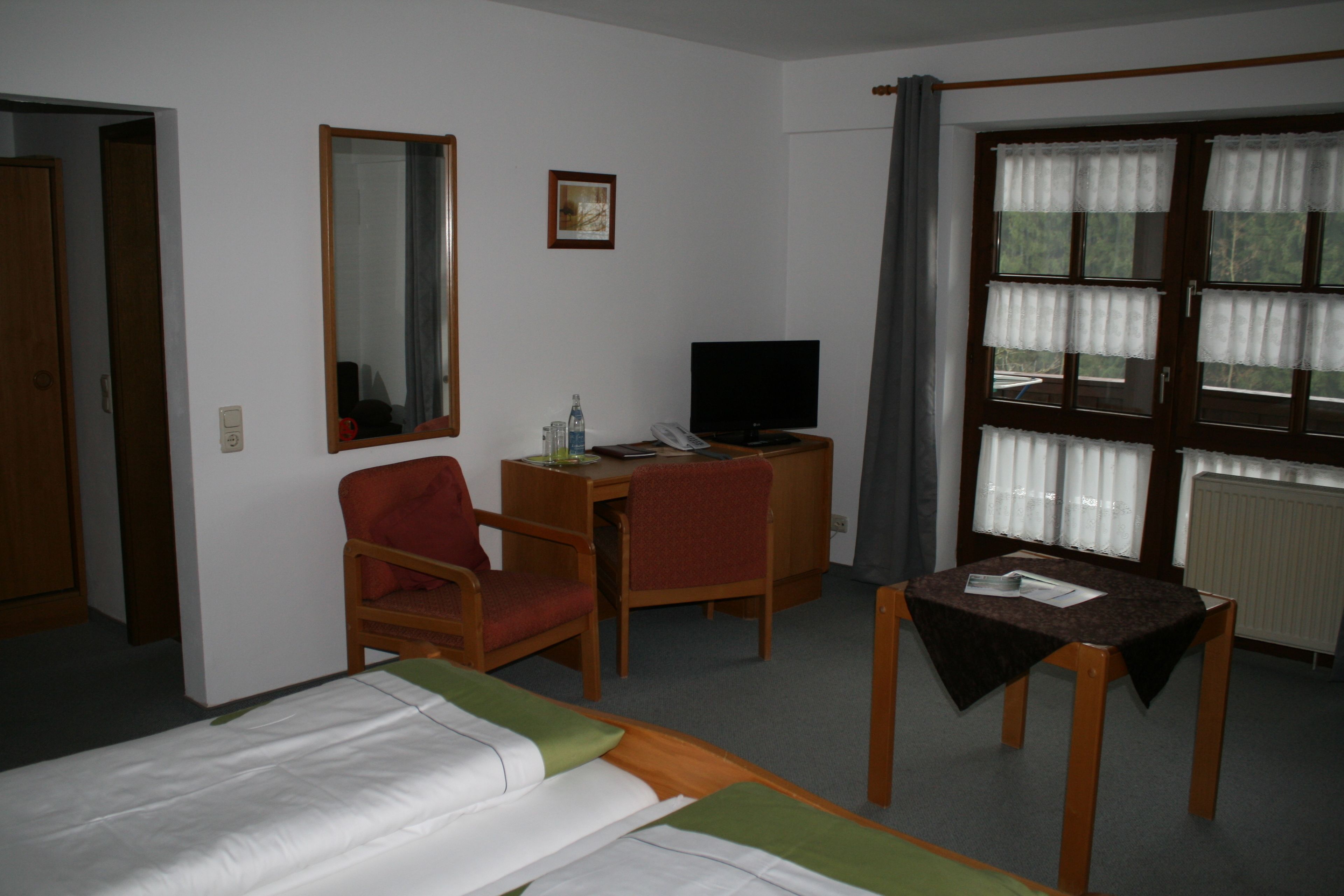 A hotel room with a bed, a desk with a computer, a chair, a television, and a window with curtains.