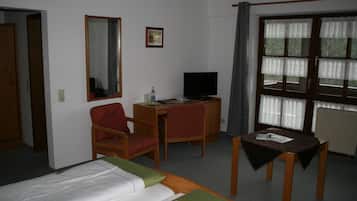 A hotel room with a bed, a desk with a computer, a chair, a television, and a window with curtains.
