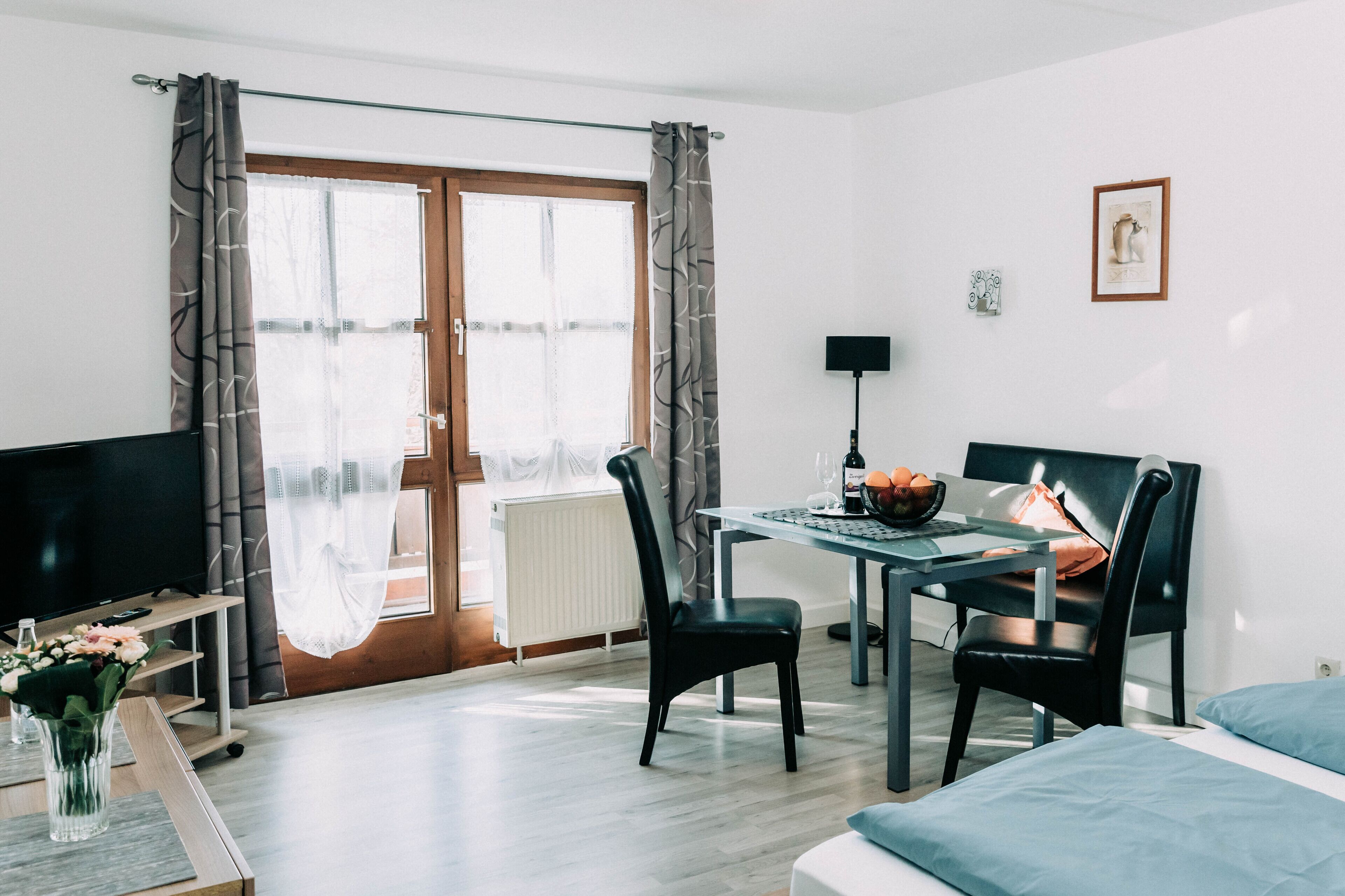 Hotelkamer met een bed, een bureau met stoel, een televisie, een eettafel met stoelen en een raam met gordijnen.