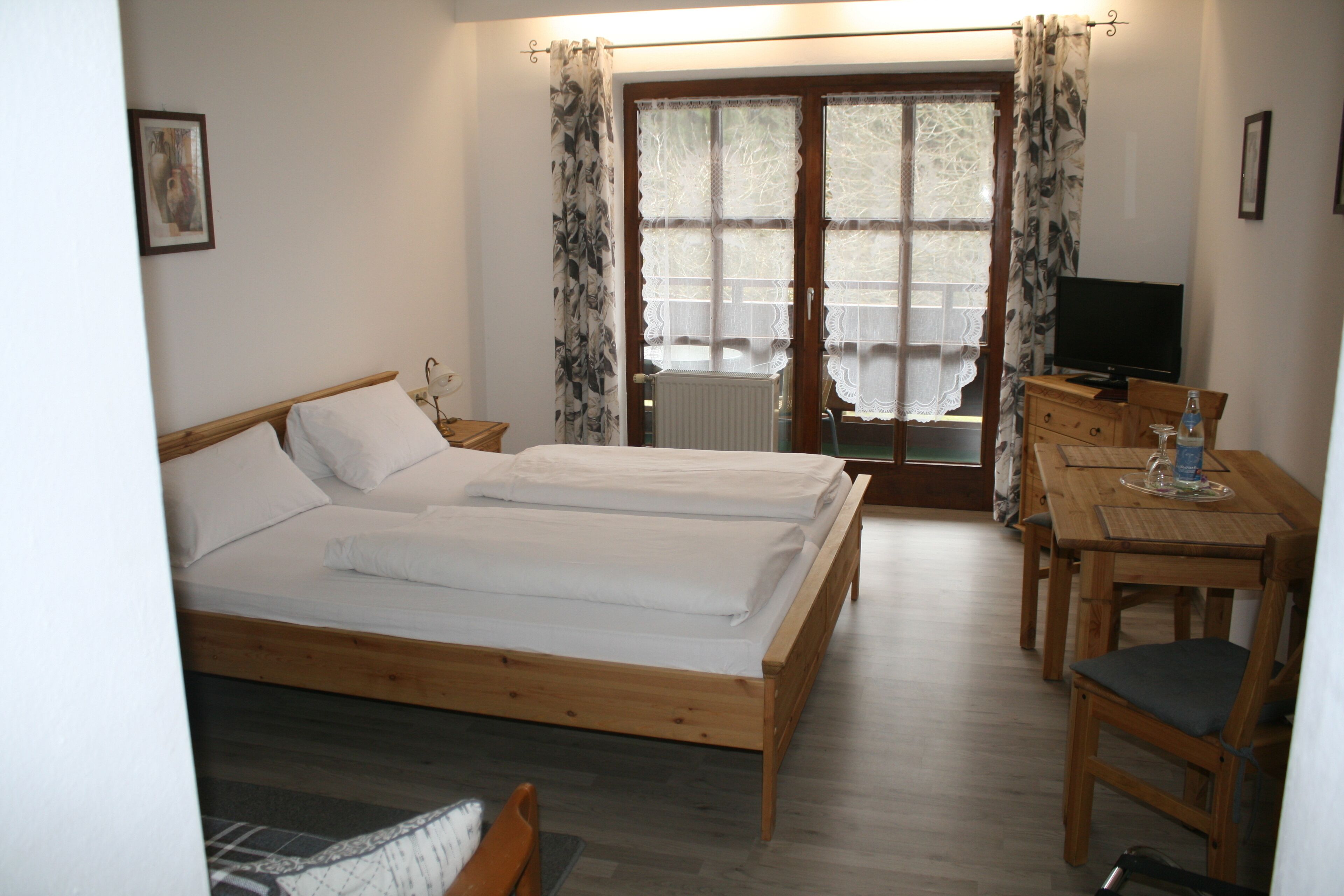 A bedroom with two beds, a wooden desk, a chair, a television, and a window with curtains.