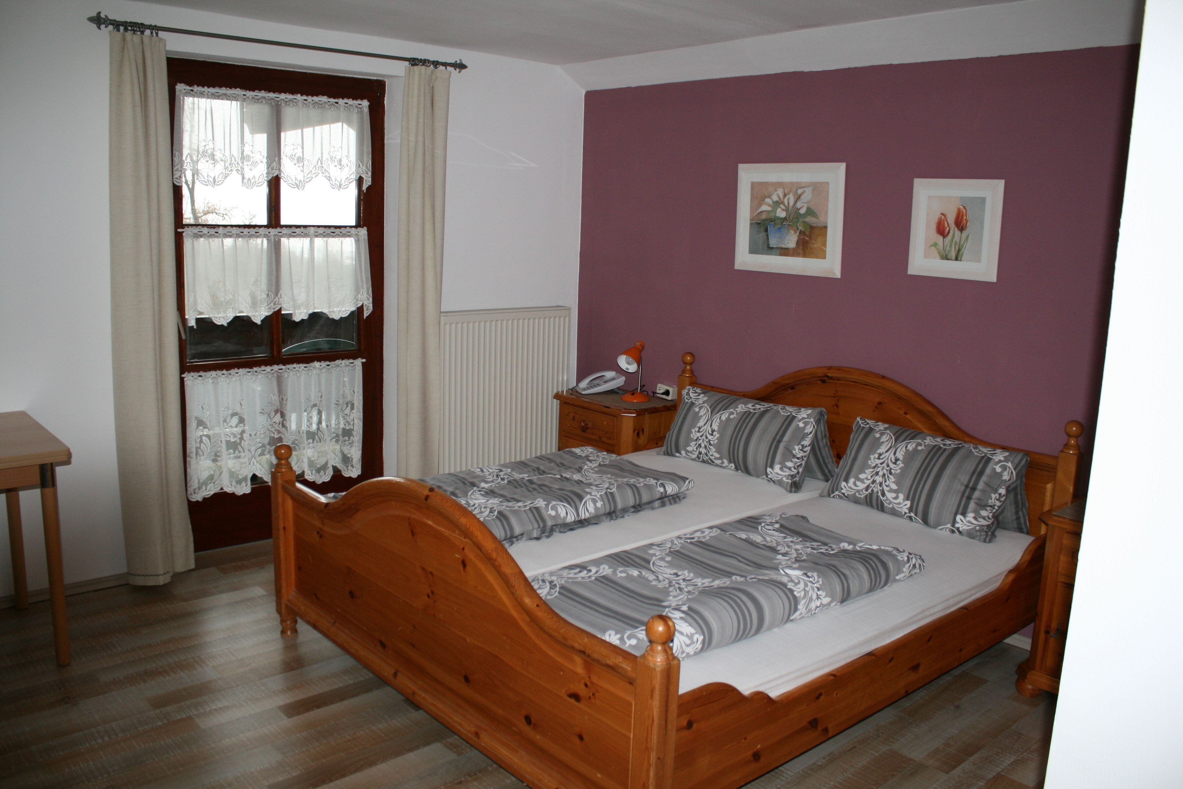 A bedroom with a wooden bed, a nightstand, a lamp, and a window with curtains.
