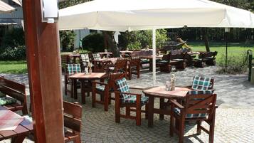 An outdoor patio area with wooden tables and chairs, covered by large white umbrellas.