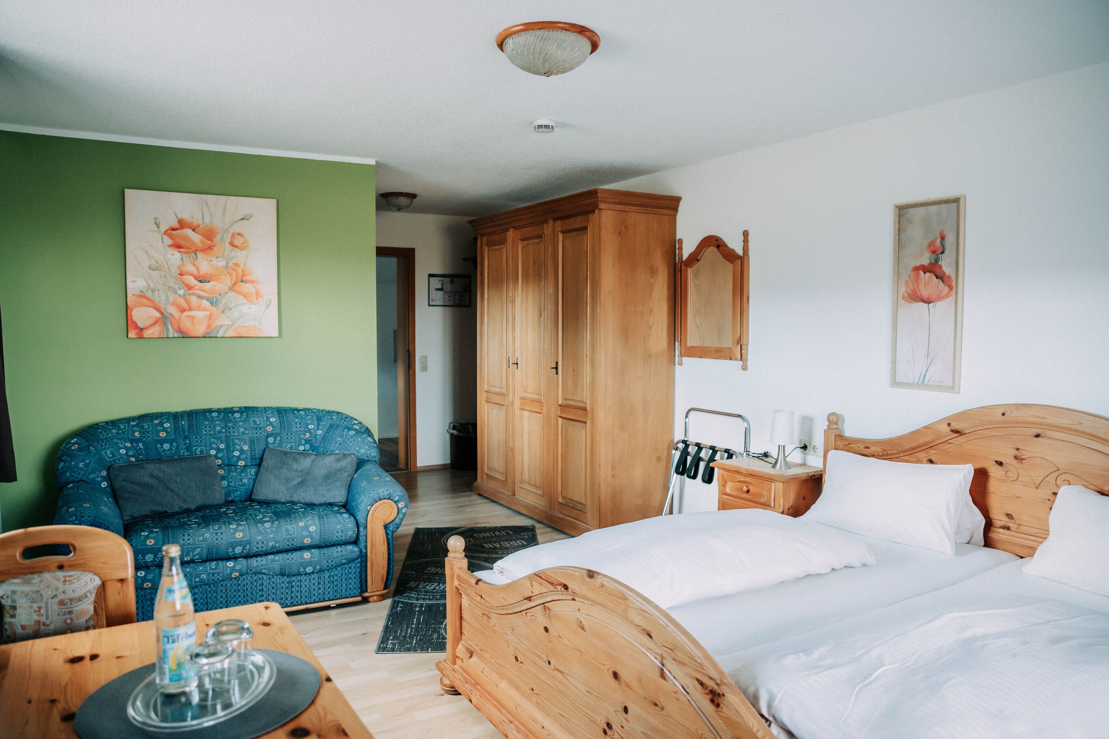 Um quarto com cama de madeira, sofá azul estampado e guarda-roupa de madeira.