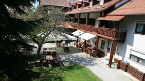 A courtyard with outdoor seating, a tree, and a building with a balcony. - Waldpension Jägerstüberl (Bad Griesbach im Rottal)