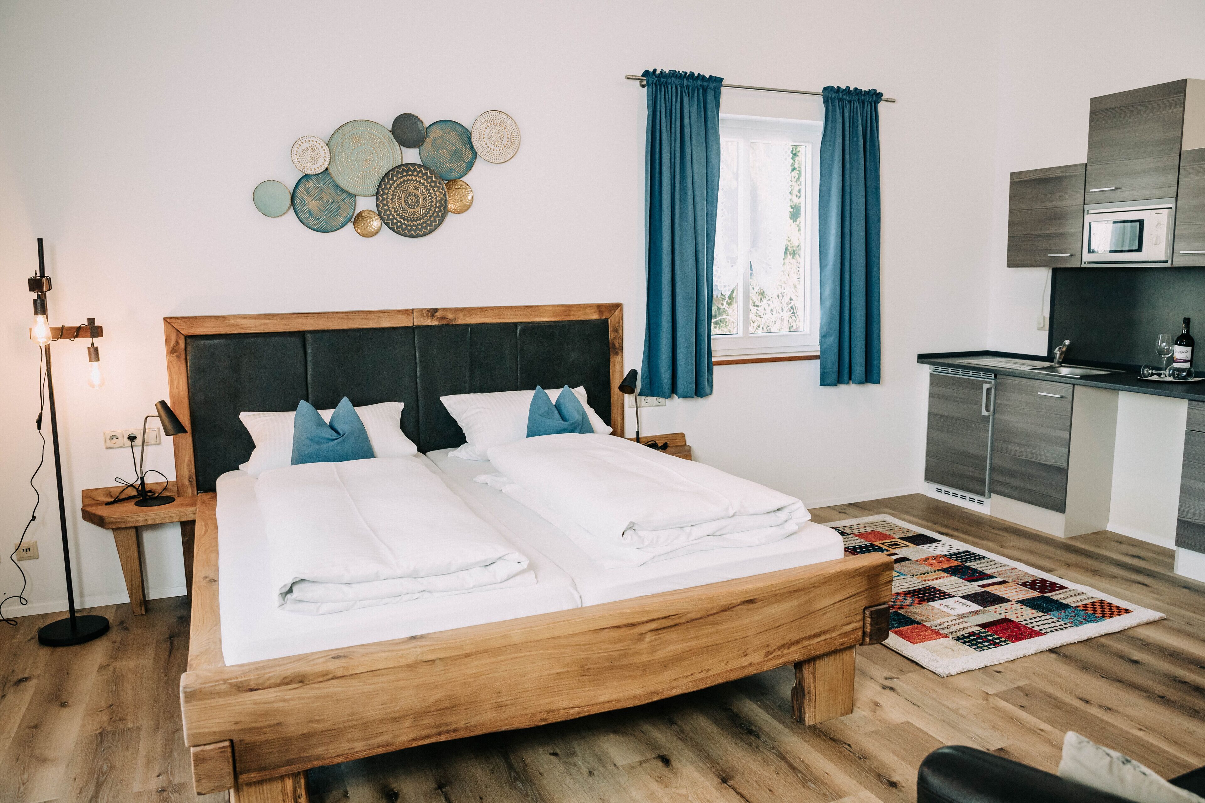 A neatly made bed with white linens, a wooden headboard, and a blue and white patterned rug.