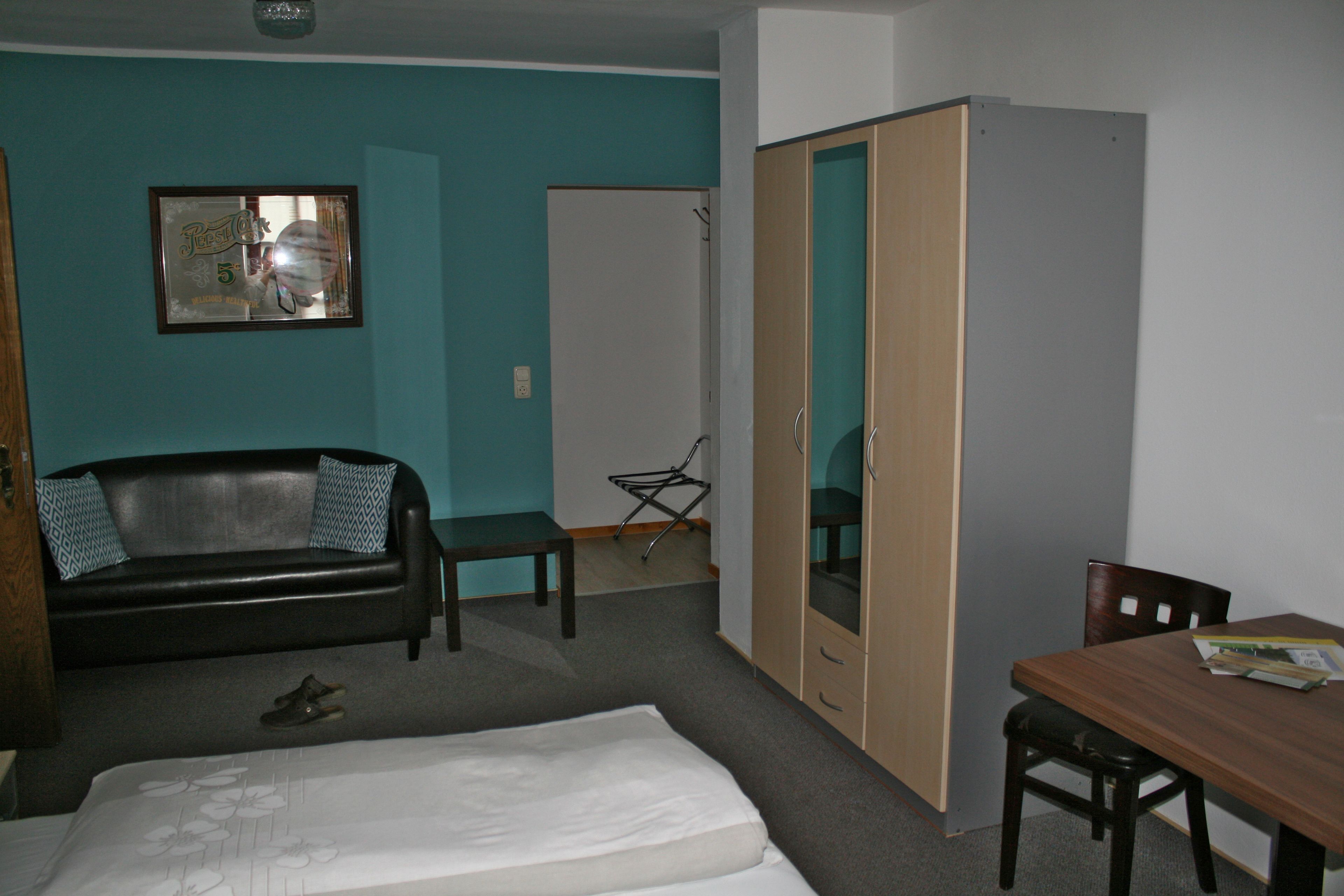 Una stanza con un letto, un tavolo in legno, un divano in pelle nera, un armadio in legno e un quadro appeso al muro.