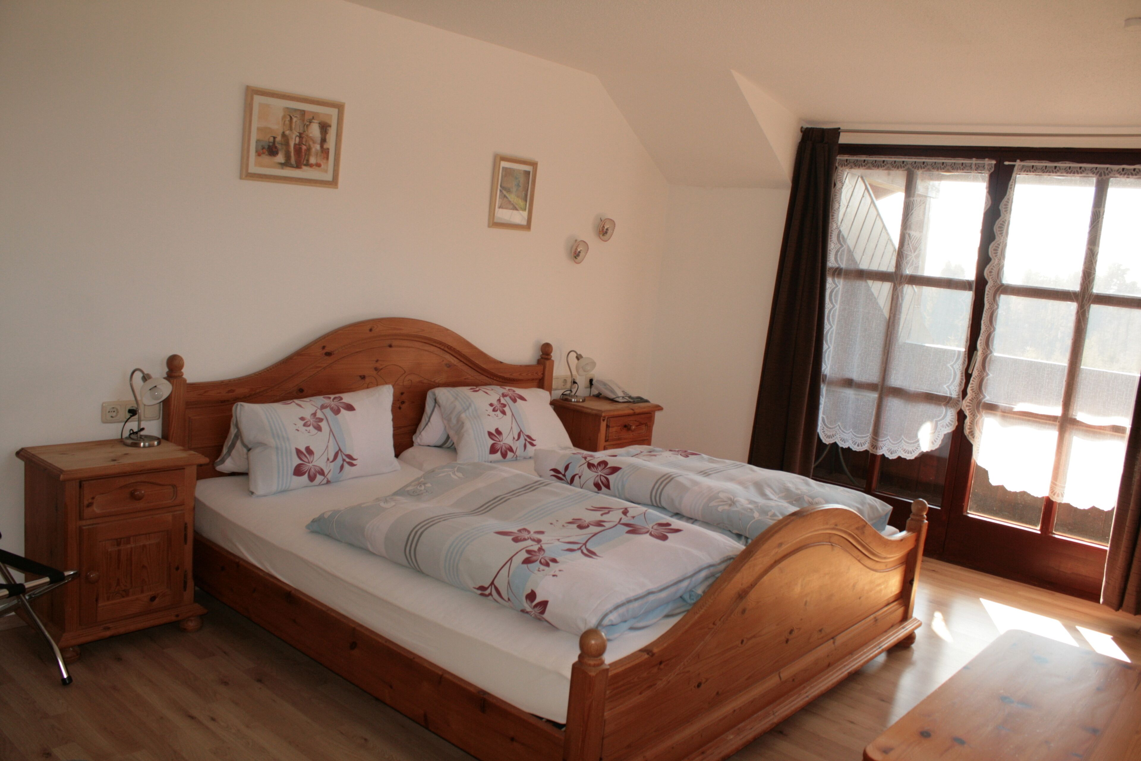 A bedroom with a wooden bed, two bedside tables, a nightstand, and a window with lace curtains.