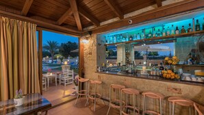 Zona de bar con taburetes, una barra llena de botellas y vistas al exterior.