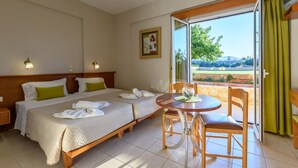 Una habitación de hotel con dos camas, una mesa de comedor y vistas al exterior.