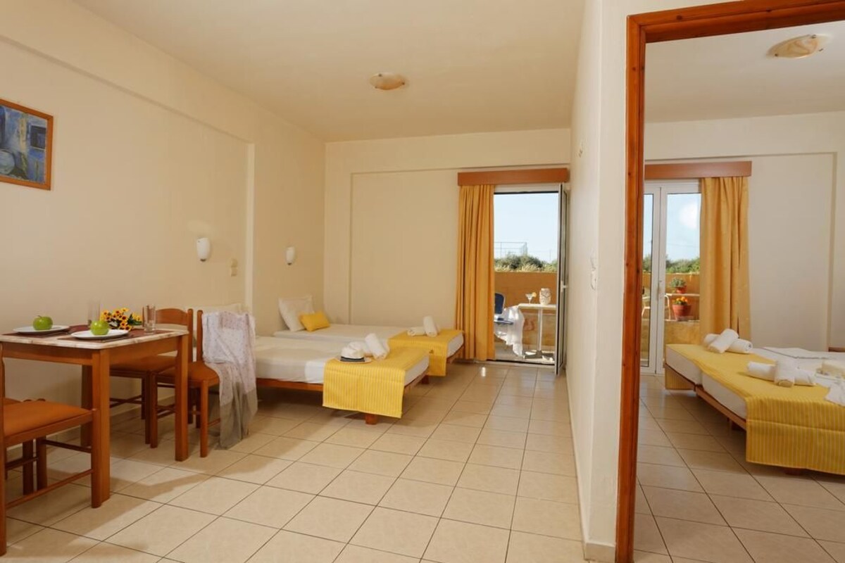 A hotel room with two single beds, a dining table with chairs, and a view of the outdoors through a glass door.