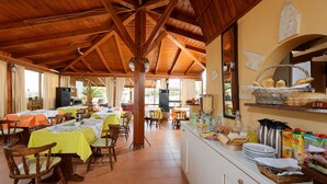 Un restaurante con vigas de madera, mesas con manteles amarillos y un mostrador de buffet con comida y bebidas.