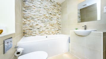 Une salle de bain moderne avec un mur recouvert de mosaïques, une baignoire blanche, un lavabo avec un receveur et des toilettes.