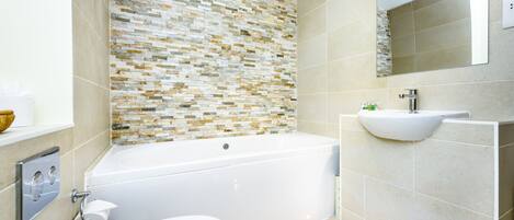 A modern bathroom with a mosaic tile wall, a white bathtub, a sink with a vessel basin, and a toilet.