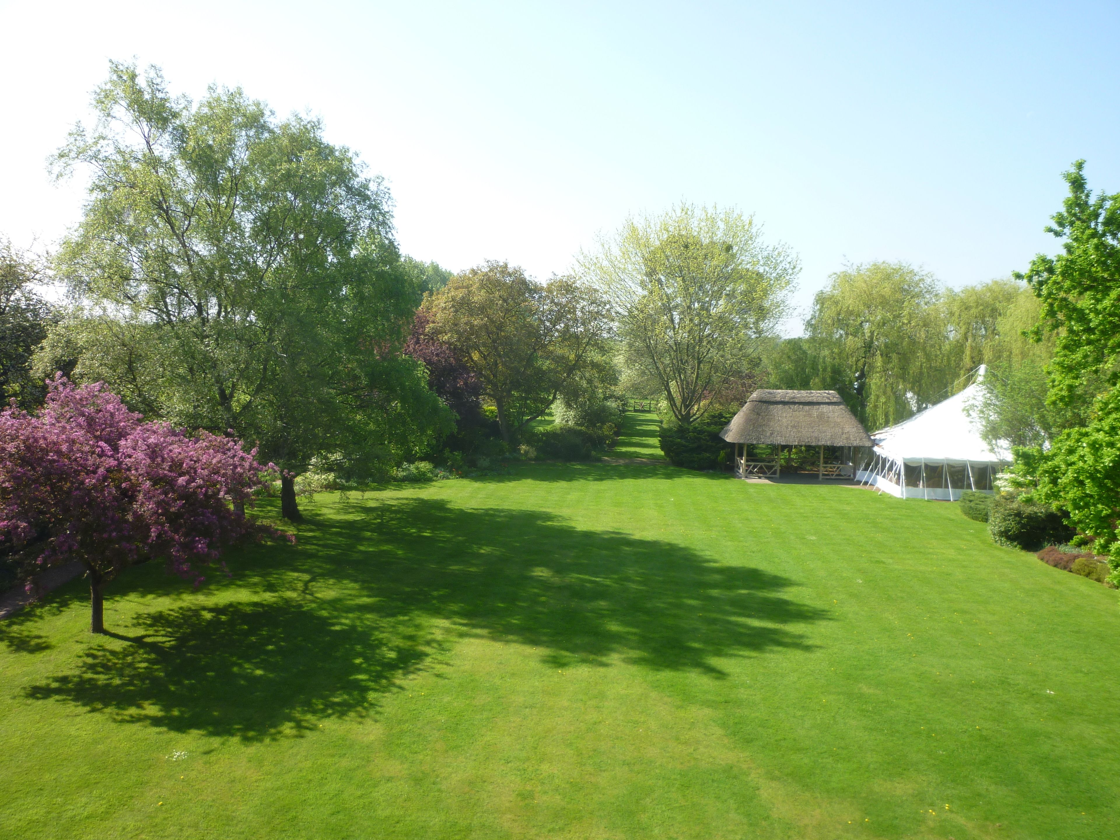 A well-maintained lawn with a thatched-roof structure, surrounded by lush greenery and trees.