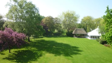 A well-maintained lawn with a thatched-roof structure, surrounded by lush greenery and trees.