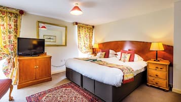 A hotel room with a bed, a television, a wooden cabinet, a nightstand with a lamp, and a patterned rug.