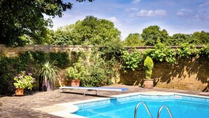 A rectangular swimming pool with metal ladders on one side, surrounded by a brick wall and lush greenery. - Rectory Farm (Cambridge)