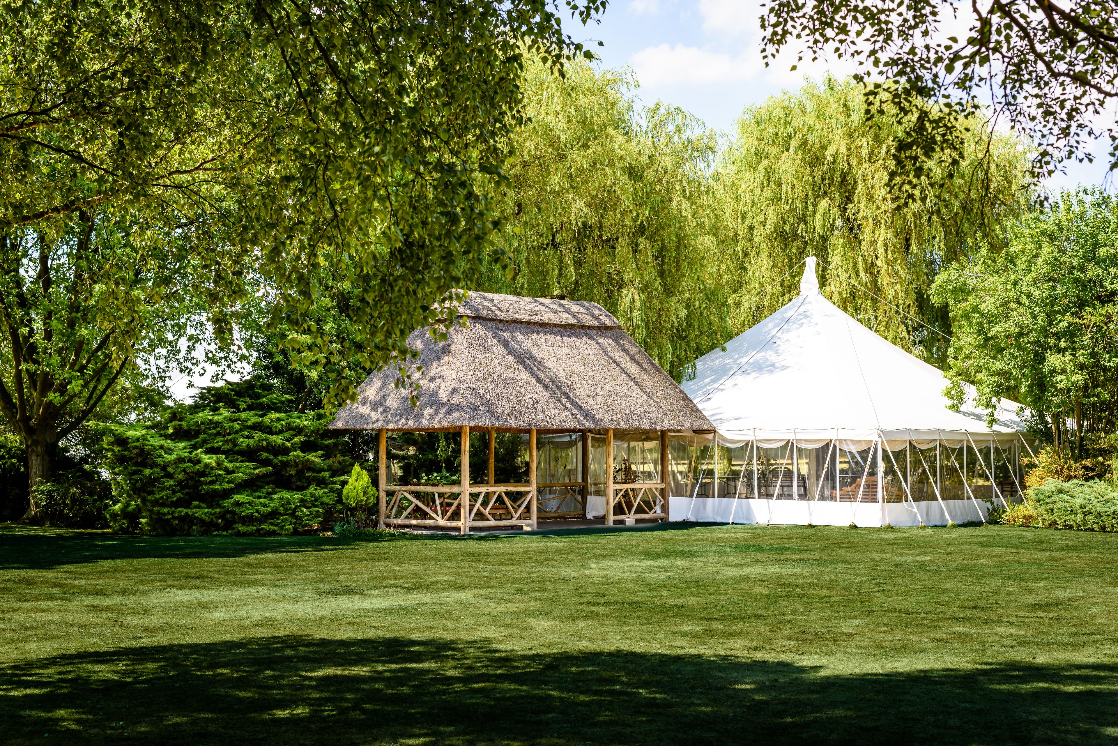 A gazebo and a tent in a park with lush greenery.