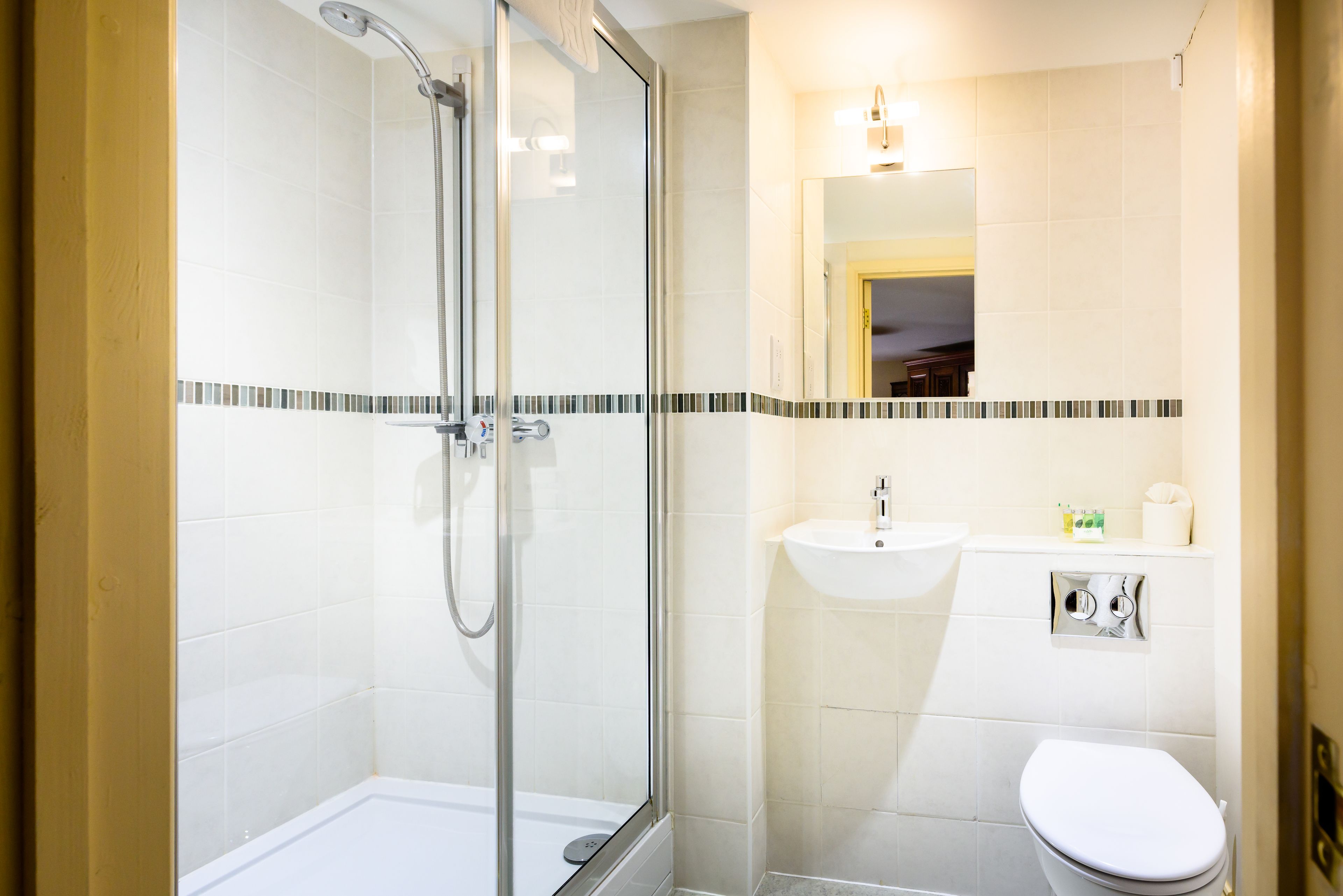 Un bany modern amb dutxa d'ús de vidre, un lavabo blanc i un vàter.
