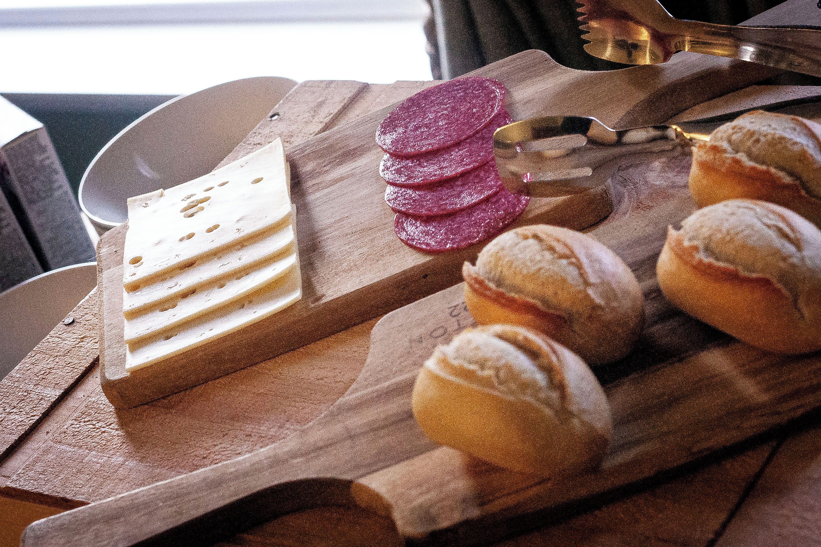 A wooden board with sliced cheese, cured meats, and pastries.