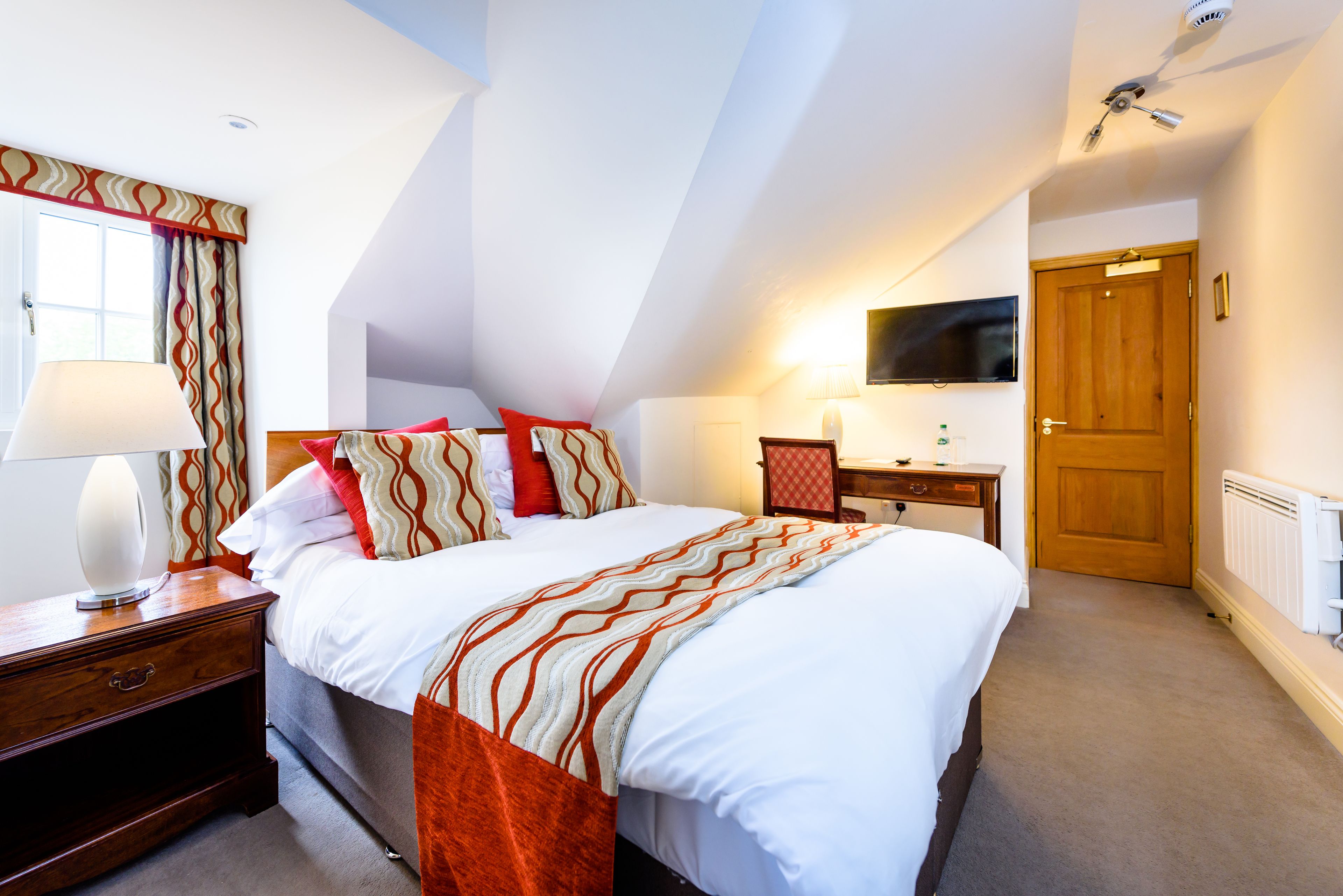 A hotel room with a large bed, a desk, a television, and a window with curtains.