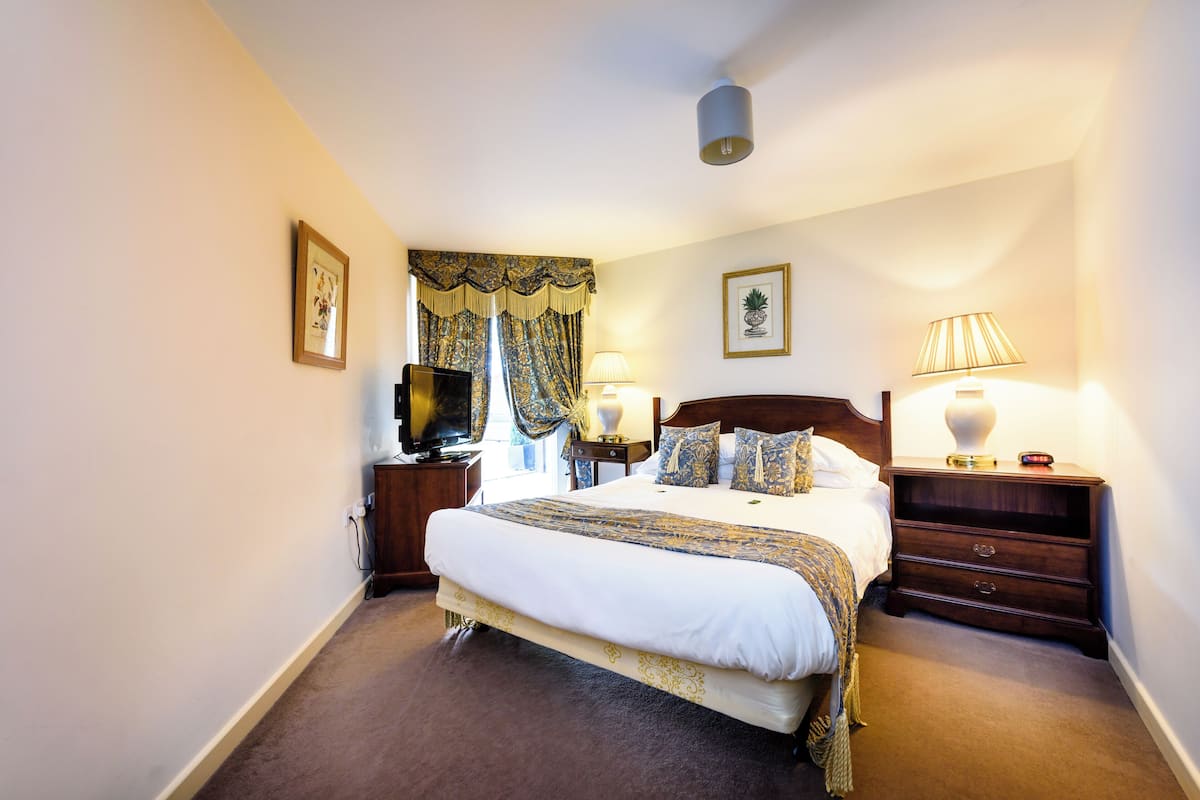 A neatly arranged hotel room with a large bed, two bedside tables with lamps, a television, and a window with curtains.