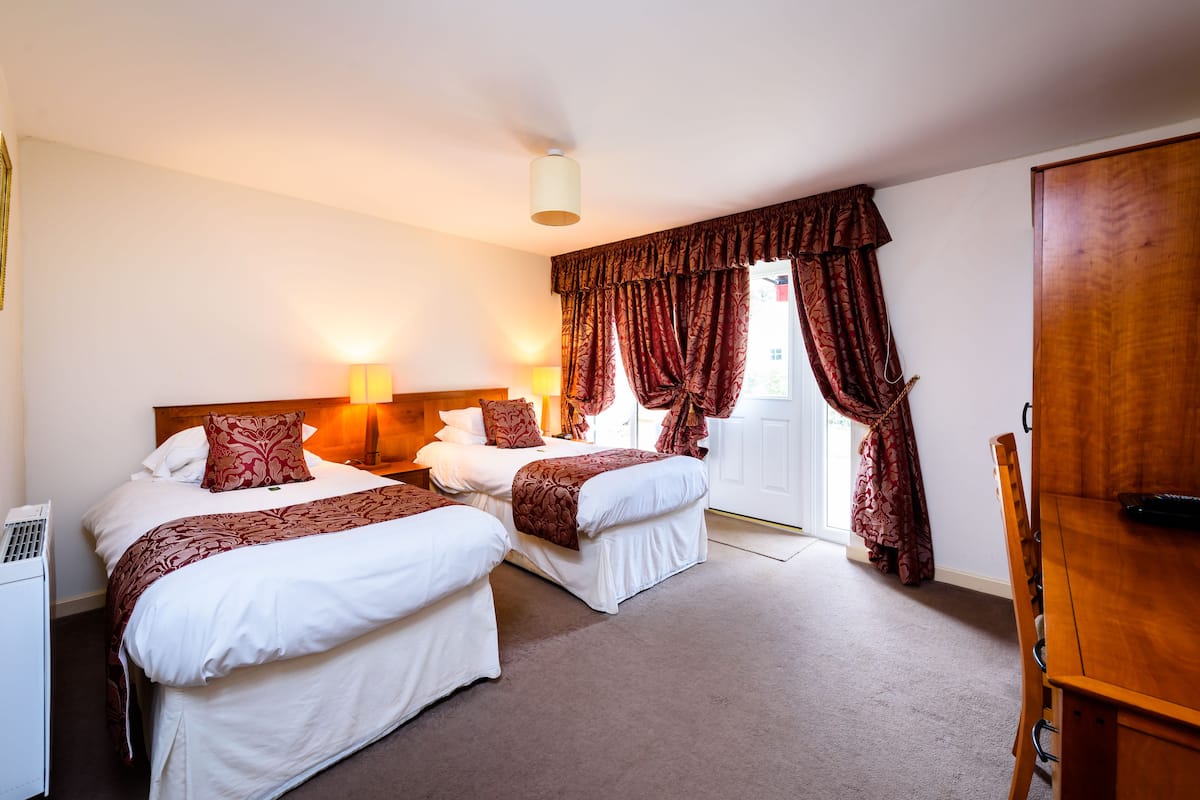 A hotel room with two beds, a wooden wardrobe, and a desk.