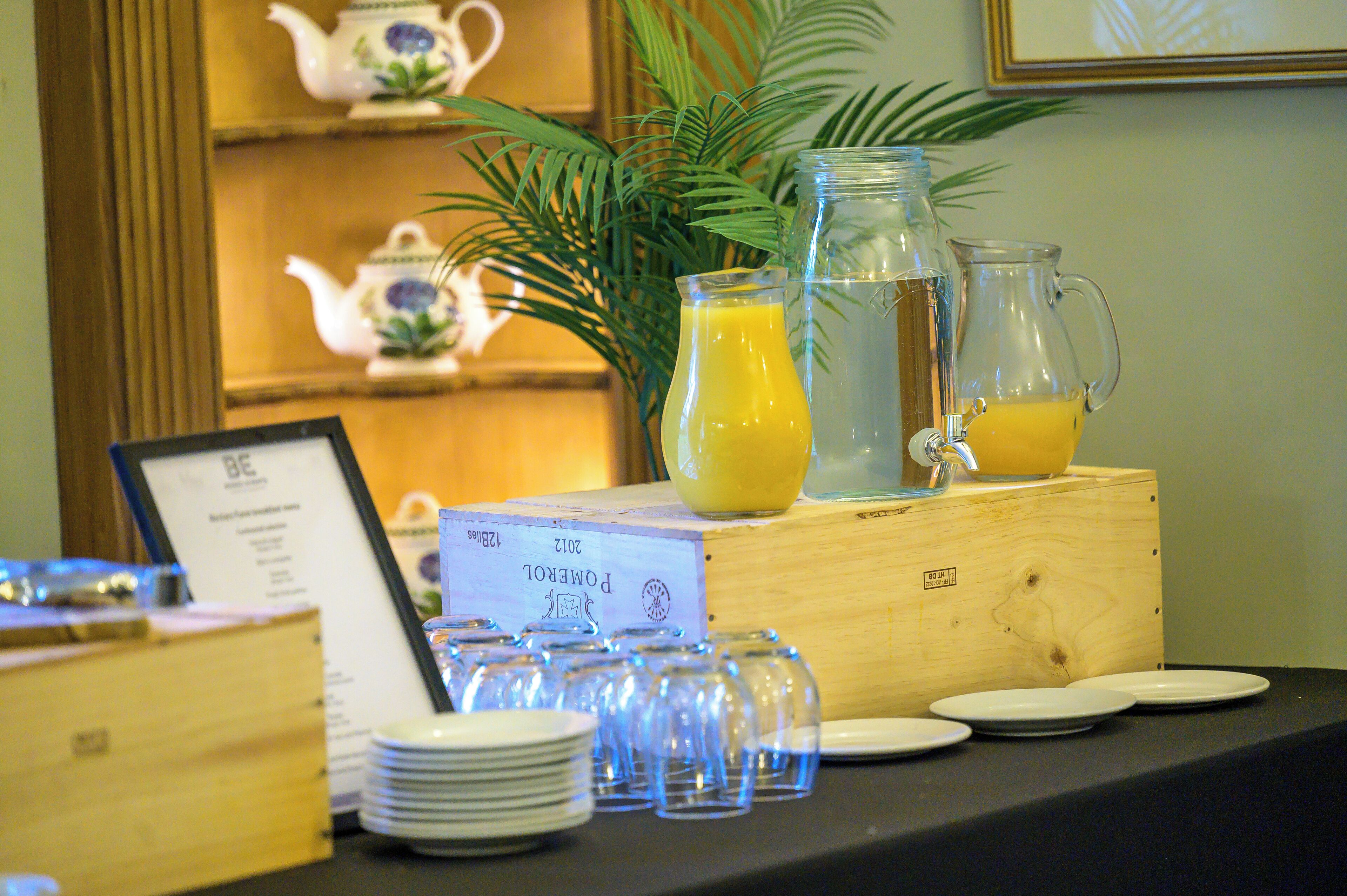 A breakfast buffet setup with a wooden table, plates, glasses, and a pitcher of orange juice.