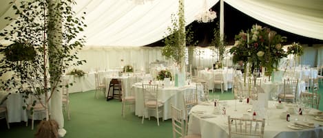 A tented event space with round tables, white tablecloths, and floral centerpieces.