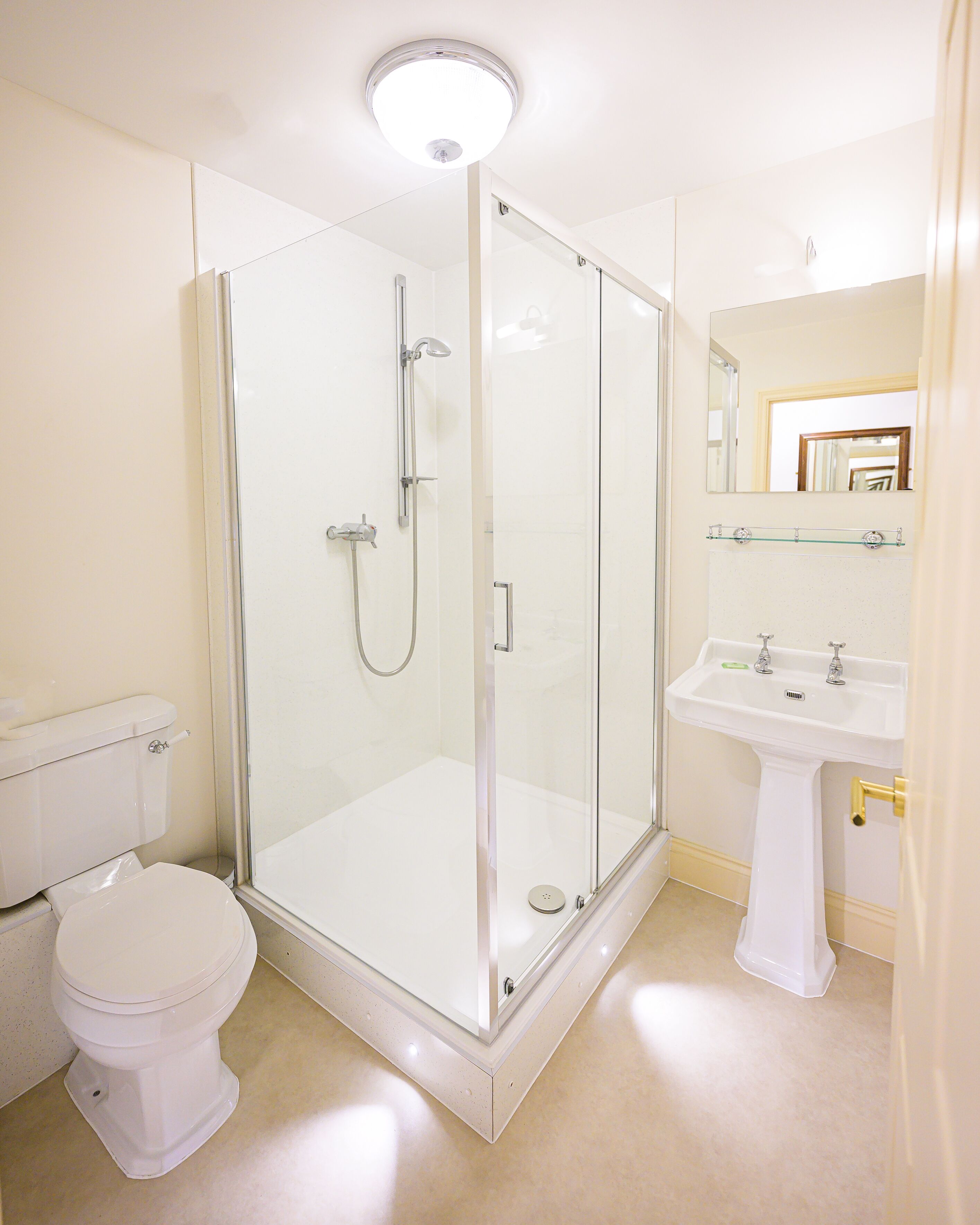 Un baño moderno con ducha de mampara de vidrio, lavamanos pedestal y retrete.