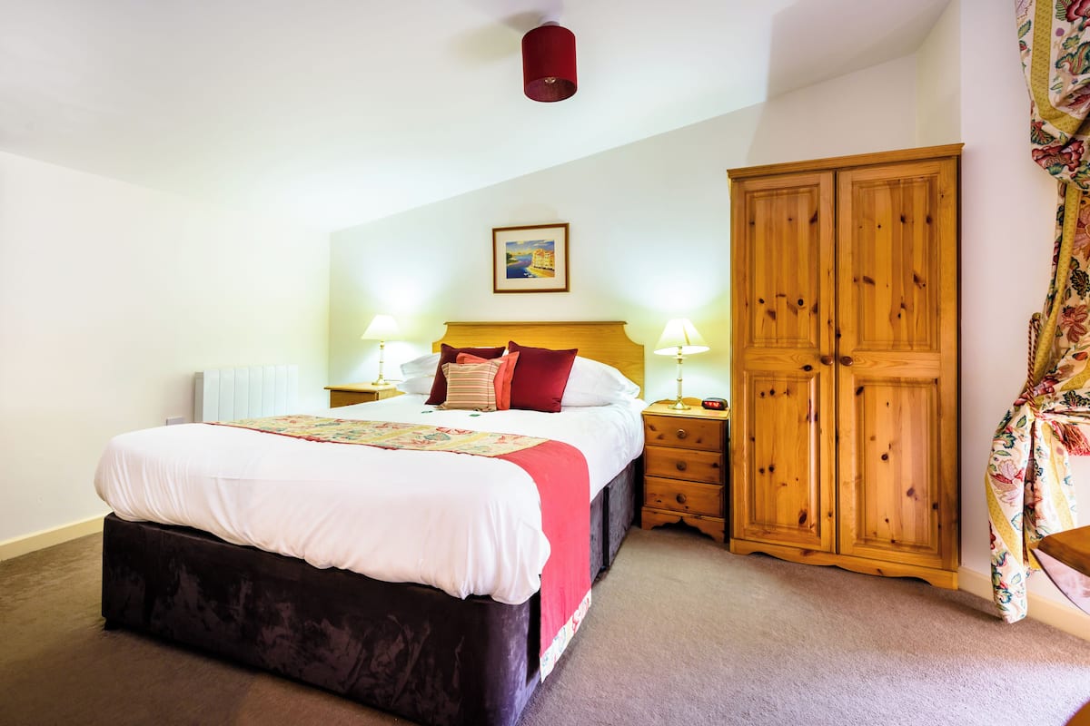 A bedroom with a large bed, bedside lamps, a wooden wardrobe, and a painting on the wall.