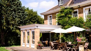 A covered patio with outdoor seating, a brick pathway, and a garden area with potted plants. - Rectory Farm (Cambridge)
