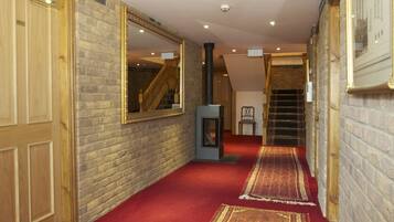 A hallway with a red carpet, a fireplace, a mirror, and a staircase.
