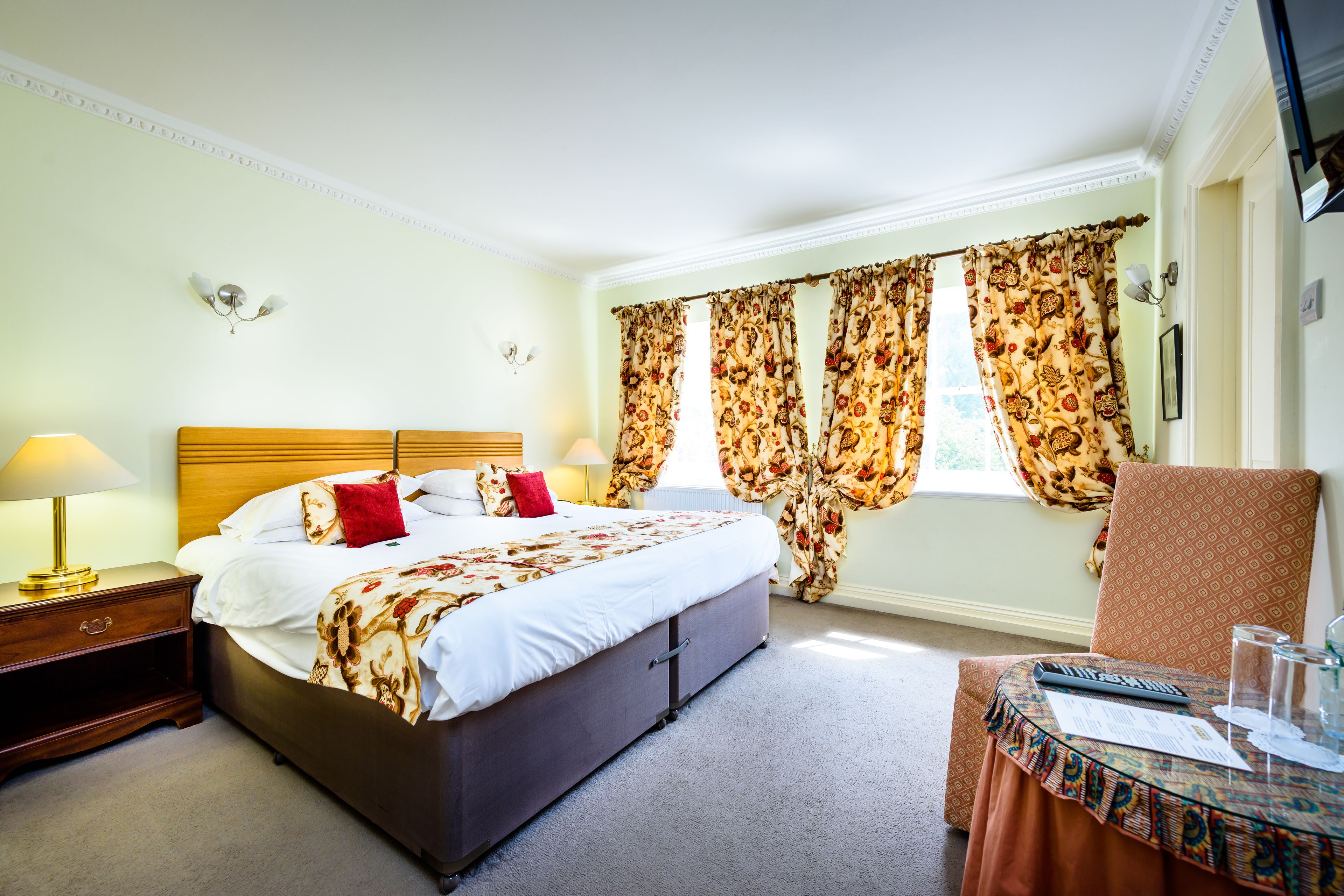A hotel room with a large bed, a nightstand, a table with a glass, and a chair.