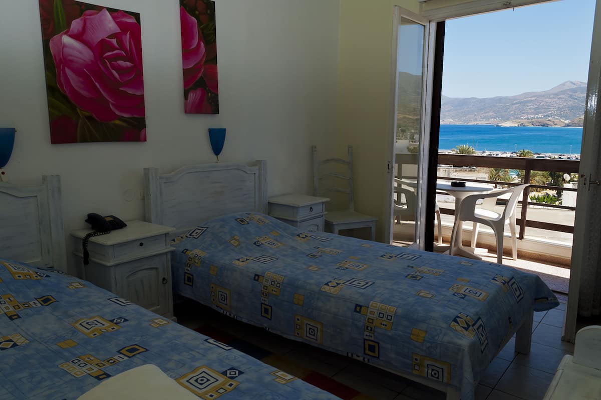A hotel room with two beds, a balcony with a view of the sea, and artwork on the wall.