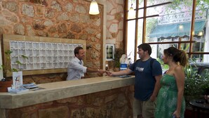 A stone counter with a display of items, a reception area with a stone wall, and a view of the street outside. - Hotel Krystal (Sitia)