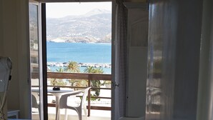 A hotel room with two beds, a small table, and a view of the sea and mountains. - Hotel Krystal (Sitia)