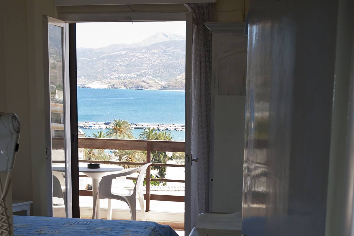 A hotel room with two beds, a small table, and a view of the sea and mountains.